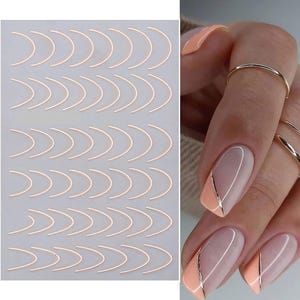 Op de afbeelding: Een vel met roségouden nail art-stickers in een gebogen vorm. De afbeelding toont ook een hand met verzorgde nagels, met een perzik- en nude-kleurenschema met een gouden streepaccent.
