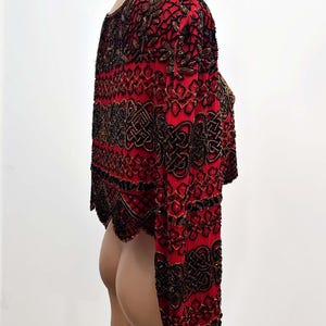 May include: A red, long-sleeved bolero jacket with intricate black and gold beadwork. The jacket features a round neckline and a cropped design. The sleeves are long and fitted, with a scalloped hemline. The beadwork creates a detailed pattern.