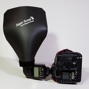 Op de afbeelding: Een zwarte flitsdiffuser met de tekst "Super-Scoop 3" en de website "www.litegenius.com" bevestigd aan een zwarte flitser op een Canon EOS camera.