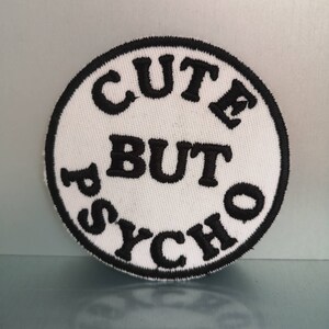 Puede incluir: Parche redondo blanco con texto bordado en negro que dice "Cute But Psycho".