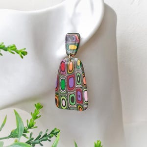 May include: Dangle earrings featuring a two-part design with a small rectangular top piece and a larger trapezoidal bottom piece. Both components display a multi-colored pattern of concentric rounded rectangles in red, orange, green, and purple.