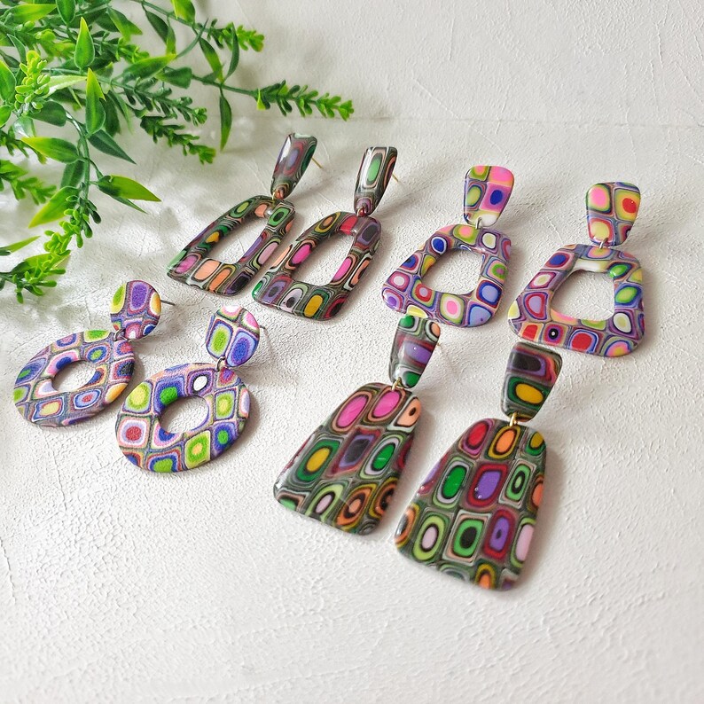 May include: Four pairs of dangle earrings featuring multi-colored geometric patterns in shades of pink, green, purple, orange, and yellow. The set includes rectangular, circular, trapezoidal, and rounded square shapes with a smooth finish.