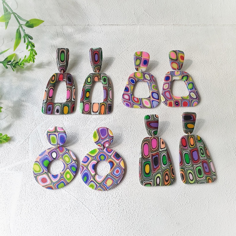 May include: Three pairs of dangle earrings featuring multi-colored, layered patterns. One pair has trapezoidal shapes, one pair has circular shapes, and one pair has elongated rectangular shapes. Each earring displays a vibrant, swirling design.