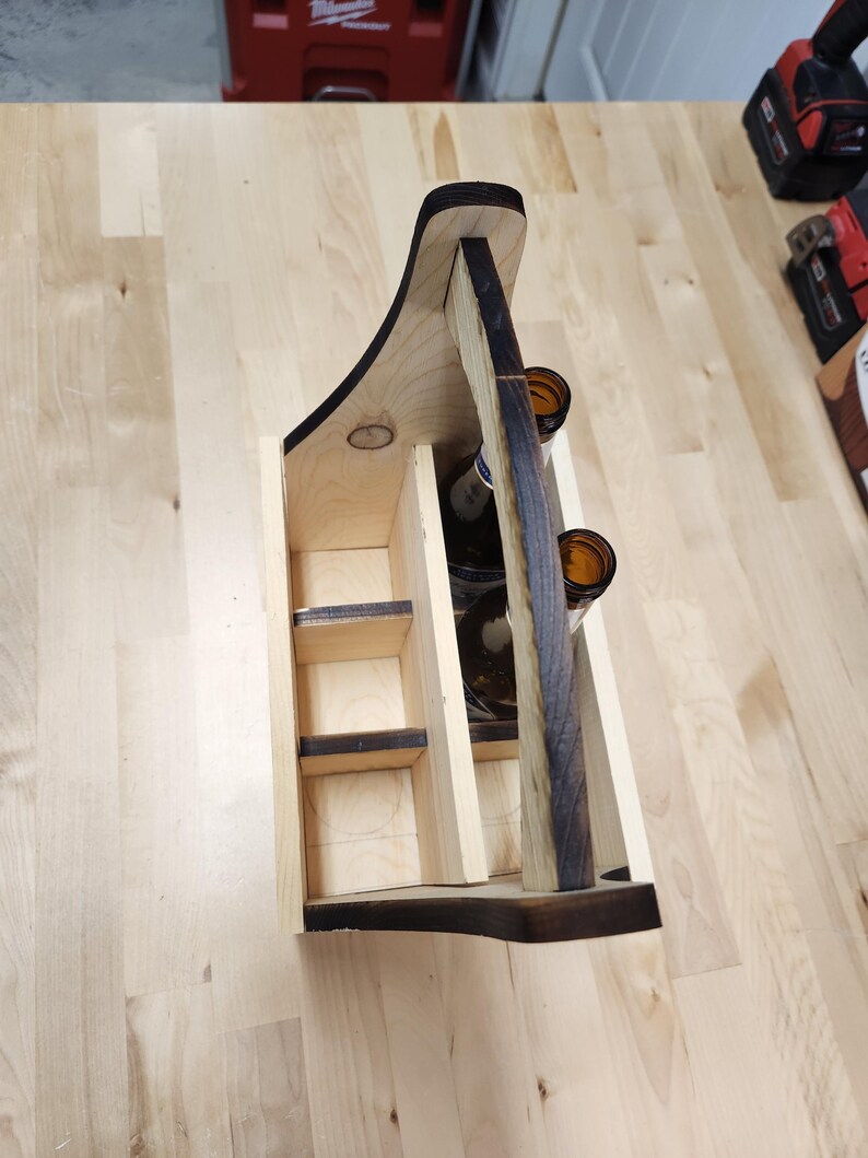 Puede incluir: Cesta de cerveza de madera con asa, dise&ntilde;ada para seis botellas. La cesta est&aacute; hecha de madera clara con detalles en marr&oacute;n oscuro de una t&eacute;cnica de quemado. El asa tiene un dise&ntilde;o curvo para facilitar el transporte. La cesta est&aacute; vac&iacute;a.