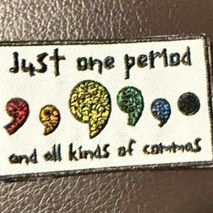 May include: A rectangular patch with the text "Just one period and all kinds of commas." The patch features a series of colorful semicolon designs in red, orange, yellow, green, blue, and black.