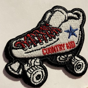 May include: White roller skate with red laces and a blue star. The skate has black wheels and the words "COUNTRY KID" are embroidered on the side.