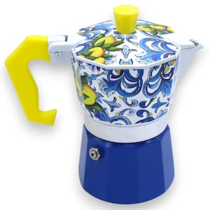 May include: A blue and white stovetop espresso maker with a yellow handle and lid knob. The coffee pot features a floral design with lemons and blue accents. The base is a solid blue color.