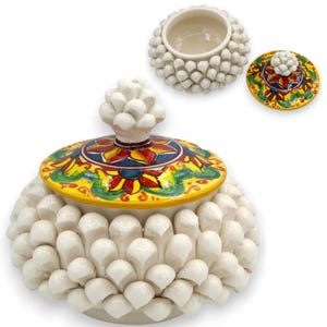 Peut inclure: Un pot en céramique avec couvercle, doté d'un extérieur texturé recouvert de protubérances blanches en forme de pétales. Le couvercle est orné d'un motif floral peint à la main en jaune, rouge, bleu et vert, surmonté d'un bouton sculpté blanc.