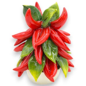 May include: A ceramic decorative plant with vibrant red, glossy chili pepper-shaped petals and green leaves. The plant is set in a cream-colored pot. The peppers and leaves have a glossy finish, creating a striking visual contrast.