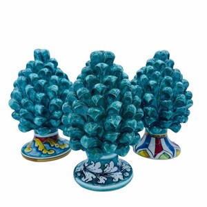 May include: Three ceramic pine cone sculptures with hand-painted details. The pine cones are teal blue and the bases are decorated with colorful floral patterns.