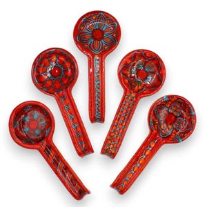 Puede incluir: Cinco reposacucharas de cerámica dispuestos en forma de abanico. Cada reposacucharas presenta un esmalte rojo brillante con patrones florales y geométricos pintados a mano en turquesa brillante y naranja. Los cuencos circulares y mangos son únicos.