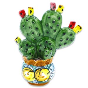 May include: A ceramic prickly pear cactus figurine featuring a vibrant green body with dark spots and small red and yellow fruit accents. The cactus is set in a round, glazed pot decorated with yellow and blue floral patterns on a white base.