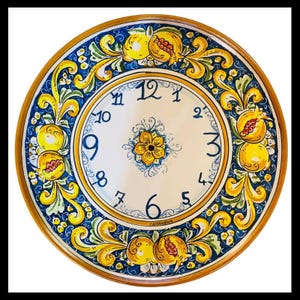 May include: A round ceramic wall clock featuring a white center with blue numerals from 1 to 12 and a central yellow flower motif. The border displays a vibrant pattern of yellow pomegranates and green leaves against a deep blue background.