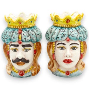 Puede incluir: Dos jarrones de cerámica con forma de rostro, uno con bigote y otro con pintalabios rojo. Ambos tienen un turbante azul, una corona amarilla y joyas doradas y rojas. Los jarrones son decorativos.