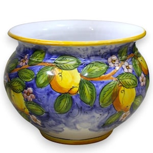 May include: A ceramic planter with a blue background and a hand-painted design of yellow lemons, green leaves, and small pink flowers. The rim is white with a yellow border. The planter has a rounded shape.