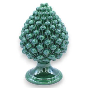 Puede incluir: Una escultura de cerámica de color verde oscuro brillante con forma de piña. El objeto presenta una superficie texturizada y estratificada con escamas redondeadas y superpuestas, apoyada sobre una base circular lisa y esmaltada.