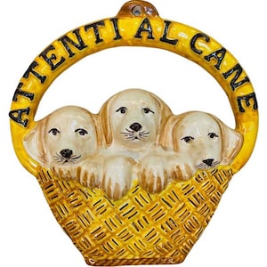 Può includere: Un cartello in ceramica gialla con il testo "Attential Al Cane" in lettere nere. Tre cuccioli di ceramica sono in un cesto di vimini giallo.