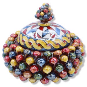Peut inclure: Un pot en céramique rond avec couvercle, doté d'un extérieur texturé recouvert de petites sphères brillantes et multicolores dans des tons de rouge, jaune et bleu. Le couvercle présente un motif géométrique en étoile et une poignée en grappe.