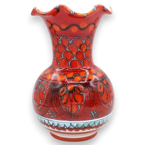 May include: A ceramic vase with a ruffled rim, featuring a vibrant orange and red base color. The surface is decorated with hand-painted patterns including teal blue scalloped lines, circular motifs, and stylized floral shapes around the body.