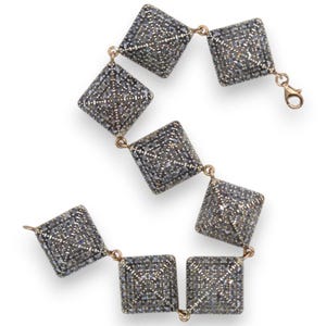 Könnte beinhalten: Ein Armband mit sieben quadratischen Gliedern mit einer texturierten, dunkelgrauen, pavé-besetzten Oberfläche. Jedes Glied ist durch kleine Metallringe verbunden, und das Stück ist mit einem goldfarbenen Karabinerverschluss zum sicheren Schließen.