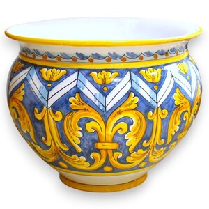 Könnte beinhalten: Ein runder Keramik-Übertopf mit handbemaltem Design, das leuchtend gelbe Schnörkel und florale Motive auf einem tiefblauen Hintergrund zeigt. Der obere Rand ist mit einer gelben Kante sowie einem blau-weißen geometrischen Zickzackmuster verziert.