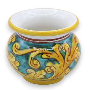 May include: A small, round ceramic pot featuring a vibrant teal background adorned with hand-painted yellow scrollwork patterns. The vessel has a wide, flared yellow rim, a white interior, and a thin brown accent line encircling the neck area.