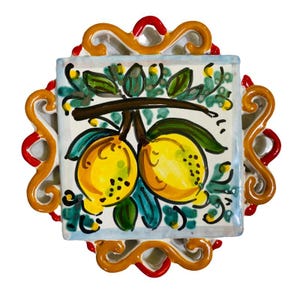 Puede incluir: Un salvamanteles cuadrado de cerámica con una ilustración pintada a mano de dos limones amarillos con hojas verdes sobre fondo blanco. El azulejo está enmarcado por un borde ornamental en forma de volutas con esmalte naranja y rojo.