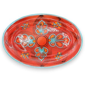 May include: An oval ceramic platter featuring a vibrant red base with a central orange circle surrounded by four symmetrical teal and orange floral-inspired motifs. The rim is outlined in a light teal border with additional small cross-hatch patterns.