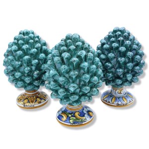 May include: Three ceramic pinecone sculptures with a glossy teal glaze. Each piece features a textured, layered scale design and rests on a circular base decorated with hand-painted yellow, blue, and white floral patterns and the text Caltagirone.