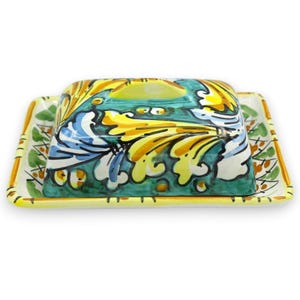 May include: A rectangular ceramic butter dish featuring a hand-painted design with vibrant yellow, teal, and white swirling leaf patterns. The lid has a central oval handle, and the base has a matching yellow and green decorative border.