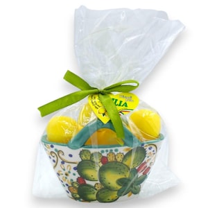 May include: A ceramic basket with a green handle and cactus design, filled with yellow lemons. The basket is wrapped in clear cellophane and tied with a green ribbon. A yellow tag with text is attached.