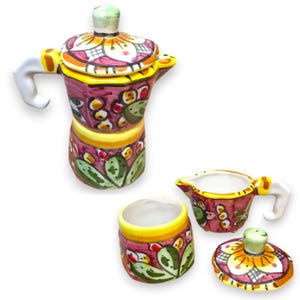 Op de afbeelding: Een keramische koffieset bestaande uit een mokapot, een melkkannetje en een suikerpot. Elk item is met de hand beschilderd met een levendig patroon van groene cactusbladeren, gele accenten en magenta bloemmotieven op een witte ondergrond.