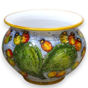 May include: A round ceramic planter featuring a hand-painted design of green prickly pear cactus pads and vibrant orange and yellow fruits against a light blue background. The rim and base are accented with a solid yellow band, and the interior is white.