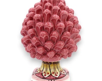 May include: A glossy ceramic pinecone sculpture featuring a vibrant pink glaze with a textured, layered scale pattern. The base is square and decorated with yellow, white, and pink floral-inspired motifs, providing a stable foundation.