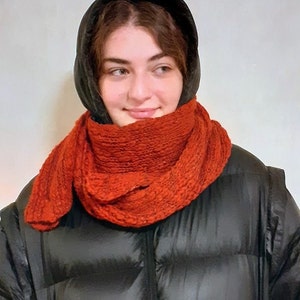 以下が含まれることがあります： 黒いフード付きジャケットと赤いニットのストールを着用した人。ストールは首と顎に巻かれている。