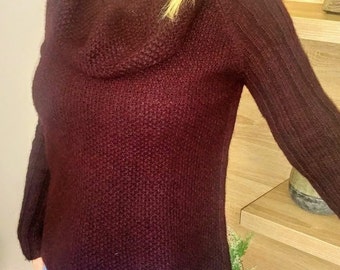 May include: A maroon cowl neck sweater with long sleeves. The sweater is made of a soft, knitted fabric.