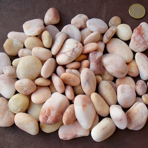 May include: A collection of smooth, light pink and cream colored river rocks. The rocks are various sizes and shapes.