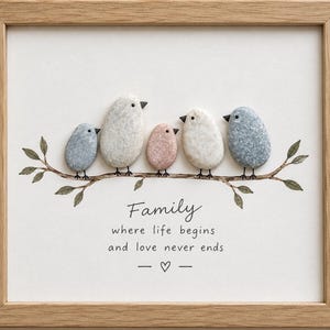 May include: A framed pebble art piece featuring five birds made of smooth stones perched on a painted branch. The text reads: Family where life begins and love never ends, with a small heart symbol below. The frame is light wood.