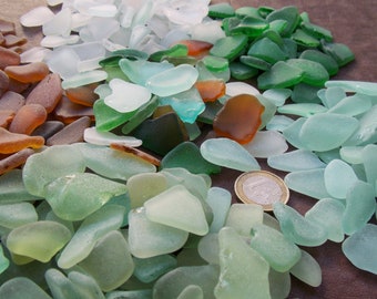 May include: A collection of sea glass in various shades of green, brown, and white. The sea glass is arranged in a pile on a brown surface. A Euro coin is visible in the center of the image.