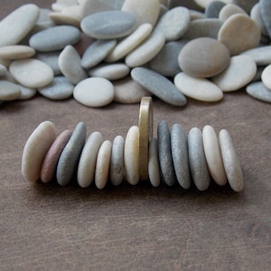 May include: A horizontal row of smooth, rounded river stones in shades of white, gray, and tan, arranged on their edges. A single gold-colored coin is inserted vertically between the stones near the center of the line.