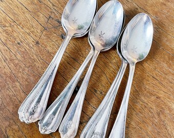 May include: Four silver spoons with ornate handles. The spoons are arranged in a row, with the handles pointing to the right. The spoons are all the same size and shape, and they have a polished finish.