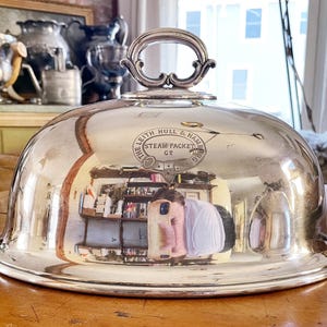 May include: A silver serving dome with a decorative handle and an inscription that reads "The Leith Hull & Hamburg Steam Packet Co."
