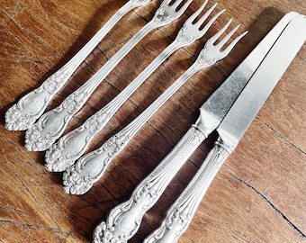 Peut inclure: Ensemble de six fourchettes en argent plaqué et un couteau assorti avec des manches ornés. Les fourchettes ont trois dents chacune et le couteau a une lame dentelée.