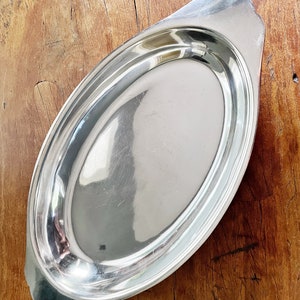 May include: A silver oval serving platter with a raised rim and two handles. The platter is made of polished metal and has a reflective surface.
