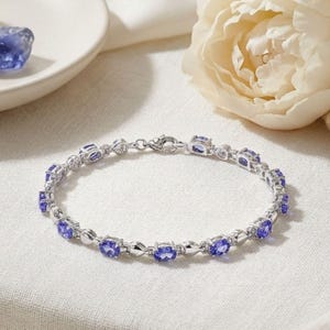 Può includere: Un bracciale a maglie color argento caratterizzato da una serie di pietre preziose ovali di un vibrante blu violaceo. Il bracciale è composto da maglie metalliche alternate e castoni, fissato da una chiusura a moschettone circolare.