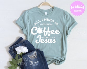 May include: A light teal t-shirt with the text "ALL I NEED IS A LITTLE BIT OF Coffee AND A WHOLE LOT OF Jesus" in white. The shirt is displayed with a pair of blue jeans and a white flower. The brand name "ALANISA BOUTIQUE" is also visible.