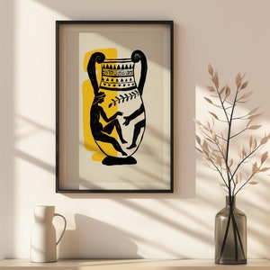 May include: Framed art print with a black frame, depicting a black and yellow illustration of an ancient Greek vase. The vase design includes figures and decorative patterns. A vase and decorative plant are in the foreground, with a neutral background.