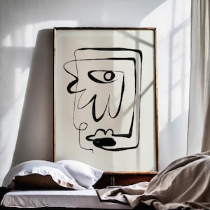以下が含まれることがあります： 白い壁に、フレームに入った抽象的な顔の白黒の線画プリント。プリントは、白と茶色の寝具を敷いたベッドの上に飾られています。