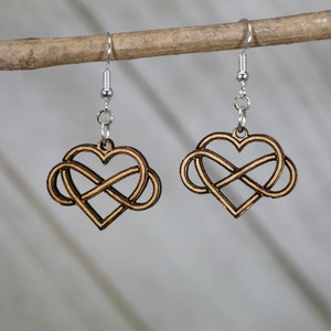 May include: A pair of wooden earrings with a heart-shaped infinity symbol design. The earrings are made of light brown wood and have silver hooks.