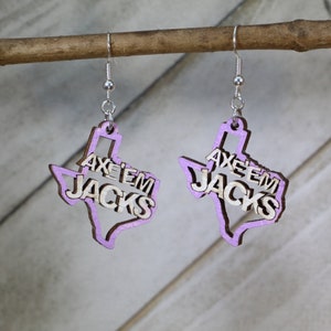 以下が含まれることがあります： 木製のテキサス州の形をした紫色のイヤリング2つ。イヤリングには「Axe 'em Jacks」という文字が刻まれています。